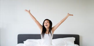 Asian Woman stretching in bed after better sleep