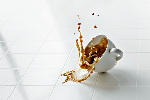 coffee cup hits white floor and spills