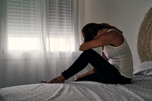 Unrecognizable abused woman sitting on her bed crying. Concept of gender violence, domestic violence and depression