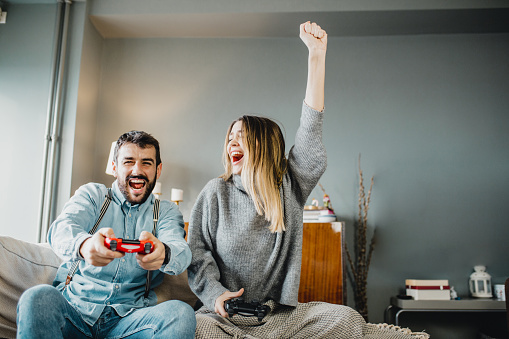 Young couple sitting on a couch in a living room and playing video games on Valentine's Day