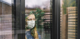 A woman wearing a mask, looking out the window during the COVID-19 pandemic