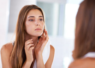 A woman looking at her features in the mirror. | Tips on how to battle Skin asthma.