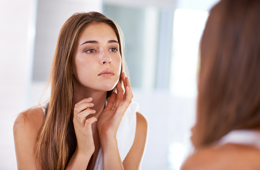 A woman looking at her features in the mirror. | Tips on how to battle Skin asthma.